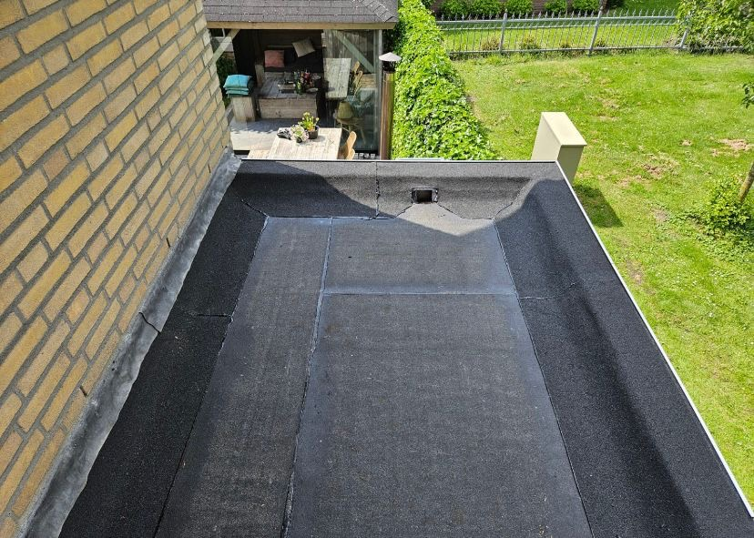 Plat dak met nieuwe bitumen dakbedekking en opstaande randen langs de gevel